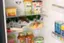 The refrigerator is filled with various food items, including a carton of eggs, a bottle of wine, and a container of hummus. There are also several bottles of juice and milk, as well as a few cans of soda. The refrigerator is well-stocked and ready for use.
