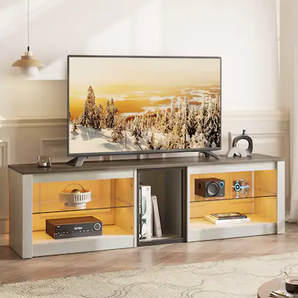 The image features a television sitting on top of a wooden stand. The TV is turned on, displaying a picture of a forest. The stand has a glass door, and there are several books and a remote control placed on it. Additionally, there is a cup and a bowl nearby, possibly for snacks or refreshments while watching TV.