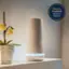 The image features a white device, which could be a router or a speaker, sitting on a shelf next to a vase with flowers. The device is illuminated with a blue light, indicating that it is functioning. The scene is set in a room with a potted plant nearby. The image is likely promoting a security system, as it is described as a "security system" and "security device."
