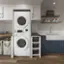 The image features a kitchen with a washer and dryer combo unit, which is the largest appliance in the room. The washer and dryer are placed next to each other, and there is a sink nearby. Additionally, there are several towels hanging on a rack above the washer and dryer. The kitchen also has a dining table and a few cups and bowls placed on it.