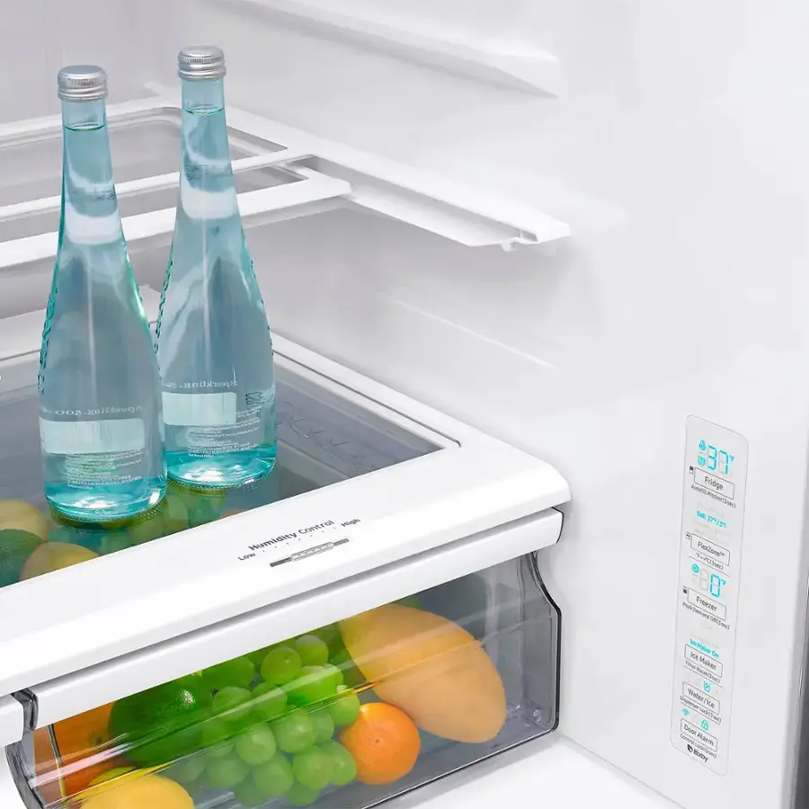 The image features a white refrigerator with two bottles of water placed on the shelves. The refrigerator is filled with various fruits and vegetables, including apples, oranges, and bananas. The fruits and vegetables are organized in the refrigerator, with some placed in the bottom drawer and others on the shelves. The refrigerator appears to be a full-size model, providing ample storage space for the items.