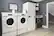 The image features a laundry room with two washing machines and a dryer. The washing machines are positioned side by side, while the dryer is located nearby. The room also includes a sink and a refrigerator. The laundry room is equipped with a television mounted on the wall, providing entertainment while doing laundry.