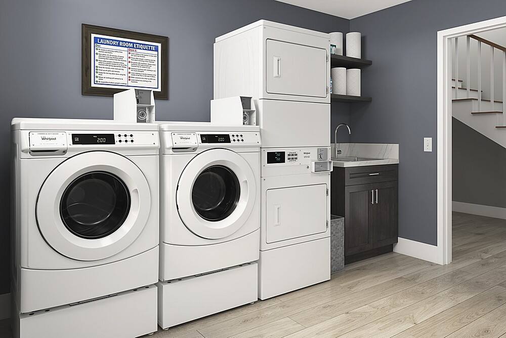The image features a laundry room with two washing machines and a dryer. The washing machines are positioned side by side, while the dryer is located nearby. The room also includes a sink and a refrigerator. The laundry room is equipped with a television mounted on the wall, providing entertainment while doing laundry.