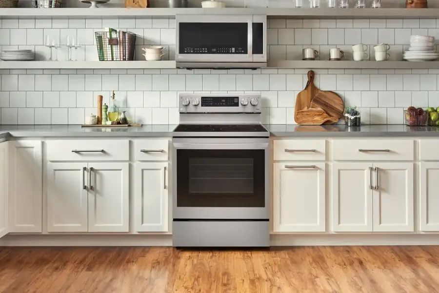 The image shows a kitchen with a stove top oven, a microwave, and a sink. The countertops are white, and there are several books and bottles placed on them. The kitchen also features a wooden floor and white cabinets.