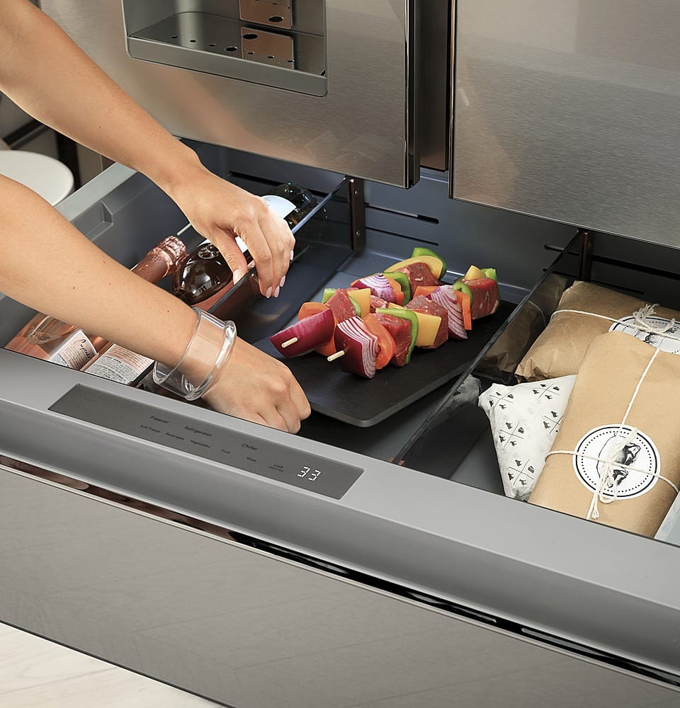 The image shows a person putting fruit into a drawer. The drawer is filled with various fruits, including apples and oranges. The person is using a knife to cut the fruits into smaller pieces, making them easier to store in the drawer. The drawer is located in a refrigerator, which is a convenient place to keep fruits fresh and easily accessible. The person is likely preparing the fruits for snacking or using them as ingredients in a meal.
