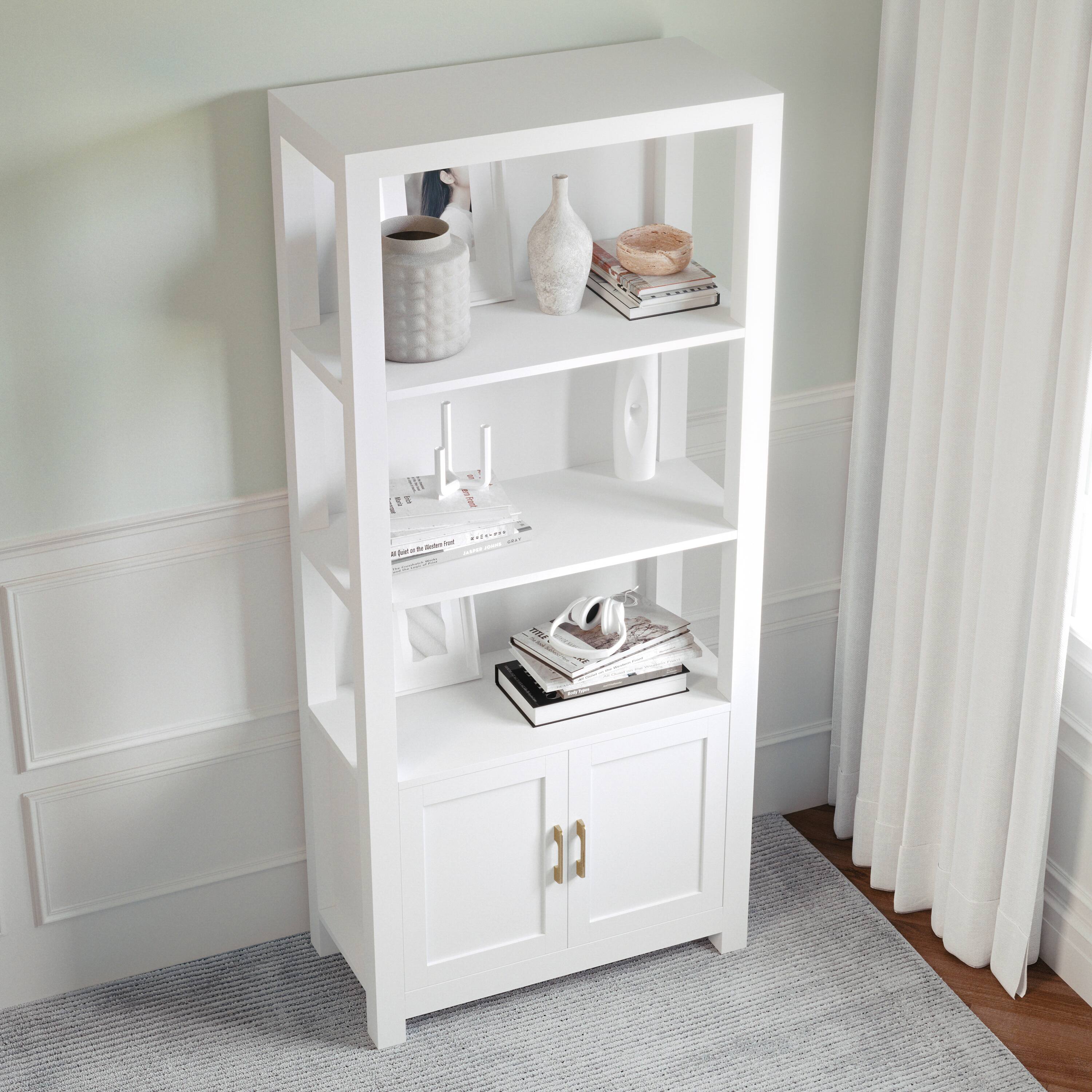 The image shows a white bookshelf with a variety of items on it. There are several books placed on different shelves, as well as a vase and a bottle. The bookshelf is situated in a room with a window, and a curtain can be seen in the background. The arrangement of the items on the bookshelf creates a visually appealing and organized space.