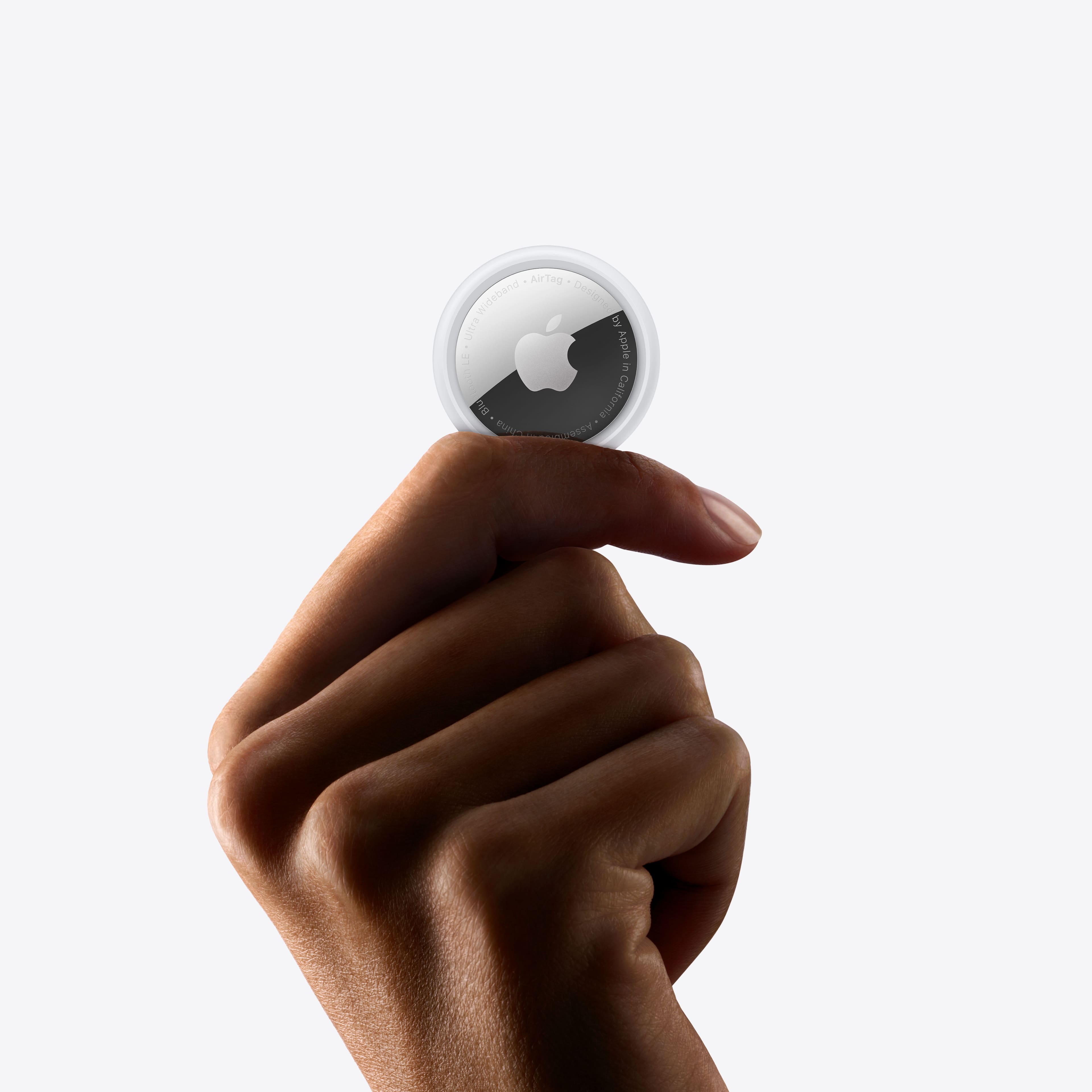 The image features a person holding a small white object in their hand, which is an AiTag. The AiTag is an item tracker that can be attached to various objects, such as keys, wallets, or bags, to help locate them easily. The AiTag is designed by Apple and is compatible with the Apple ecosystem. The person is holding the AiTag up against a white background, showcasing its size and simplicity.