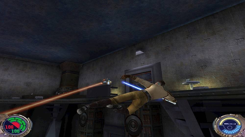 The image shows a man in a brown shirt and khaki pants, holding a blue and white lightsaber, and standing in a dark room. He appears to be playing a video game, possibly Star Wars, as he is holding the lightsaber in a ready position. The man is positioned in the center of the room, and the scene is set in a dark environment, which adds to the dramatic atmosphere of the game.