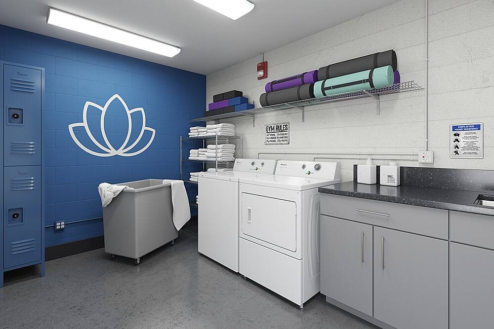 The image shows a clean and organized laundry room with a washer and dryer. There is a blue wall with a white flower on it, and a shelf above the washer and dryer. The room also has a sink and a locker. The text "GYM RULES" is displayed in the room, likely to remind users of the rules and etiquette for using the facility.