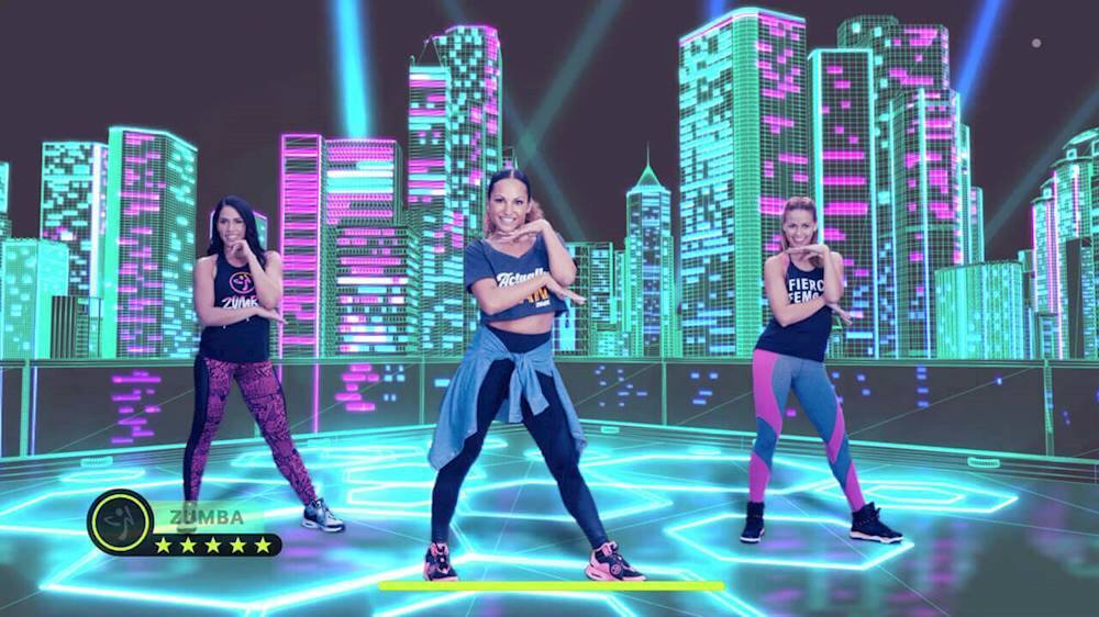 The image features three women dancing on a stage in front of a city skyline. They are performing a choreographed routine, possibly for a music video or a live event. The women are wearing tight clothing, and their dance moves are synchronized, showcasing their skills and coordination. The stage is illuminated with bright lights, creating an energetic and lively atmosphere.
