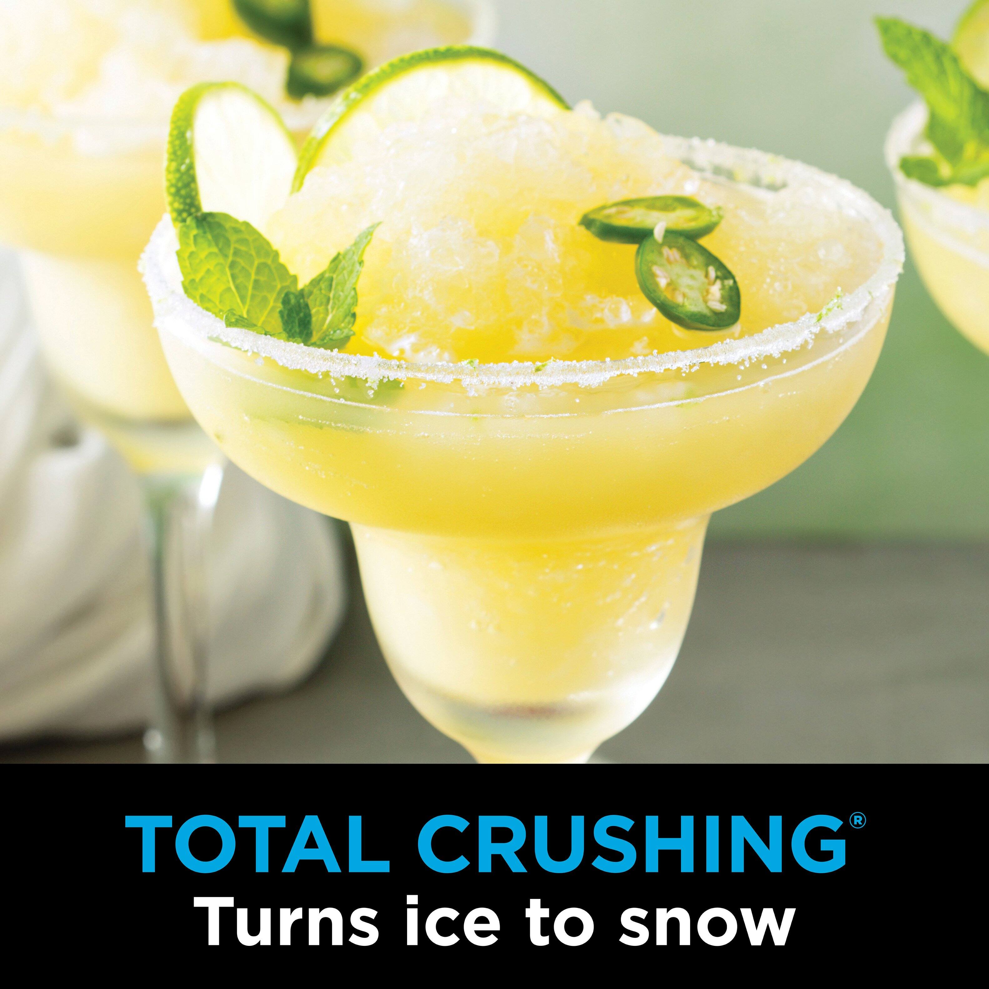 The image features a close-up of a margarita glass filled with a yellow drink, possibly a pina colada, and garnished with lime slices. The glass is placed on a table, and there are other glasses in the background. The advertisement suggests that Total Crushing turns ice to snow, possibly referring to a cooling effect or a refreshing beverage.
