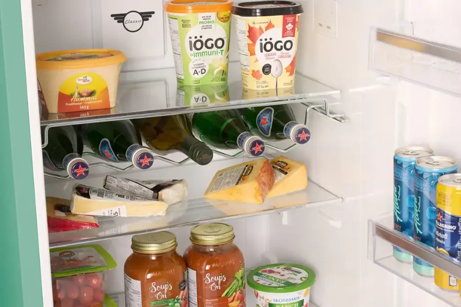 The image shows a refrigerator with various food items and drinks. The refrigerator is stocked with a variety of items, including bottles of drinks, such as water and soda, and food items like hummus, soup, and yogurt. There are also several bottles of wine and other beverages. The refrigerator is well-organized, with the items placed neatly on the shelves. The image also features a sign that says "Igogo," possibly indicating a brand or a specific product.