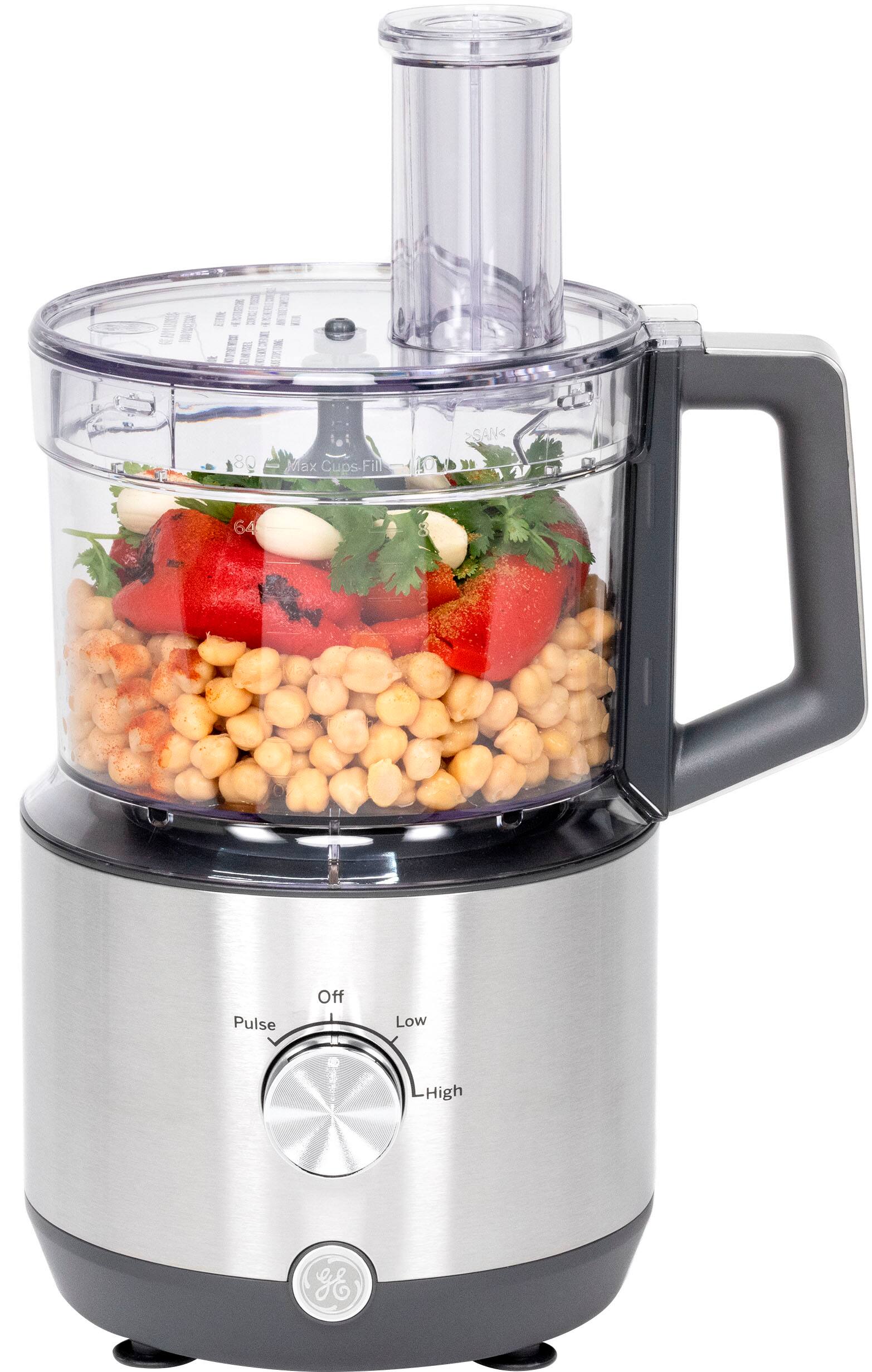 The image features a mini-chopper bowl filled with chopped nuts. The bowl is placed inside a blender, which is ready to be used. The blender has a clear glass container, allowing the user to see the contents inside. The image also includes a potted plant in the background, adding a touch of greenery to the scene.