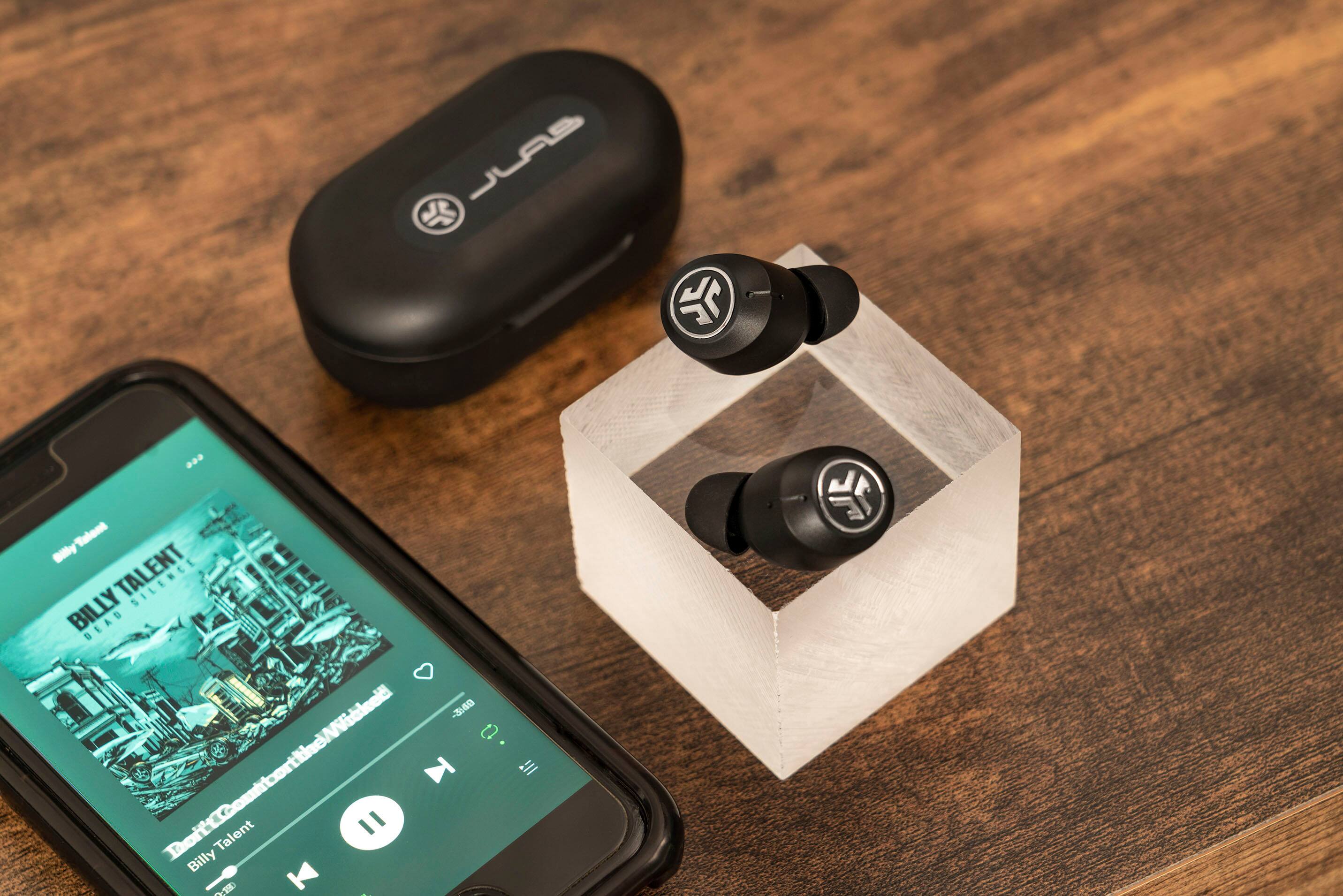 The image features a cell phone, a case, and a pair of earbuds. The cell phone is placed next to the case, and the earbuds are sitting on top of the case. The earbuds are connected to the cell phone, possibly for listening to music or making a call. The case is placed on a wooden table, providing a stable surface for the items.