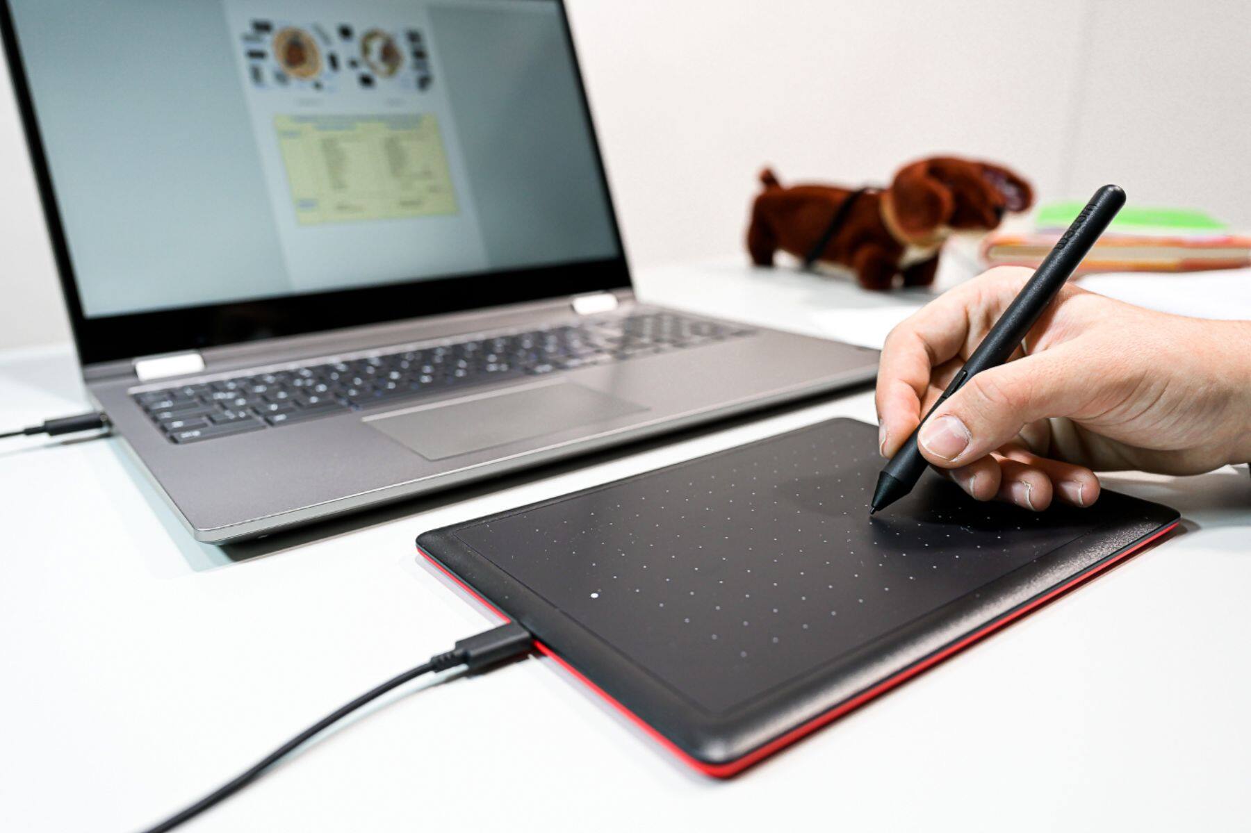 A hand writing on a black drawing tablet with a black pen in front of a black laptop on a desk