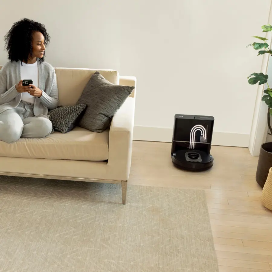 The image features a small dog sitting in a white dog bed, surrounded by a few bags and a vase. The main focus of the image is a Shark vacuum cleaner, which is designed to be perfect for homes with pets. The vacuum cleaner has powerful suction and a self-cleaning brushroll, making it effective in picking up pet hair with an anti-hair wrap. The presence of the dog and the dog bed in the image emphasizes the pet-friendly aspect of the Shark vacuum cleaner.