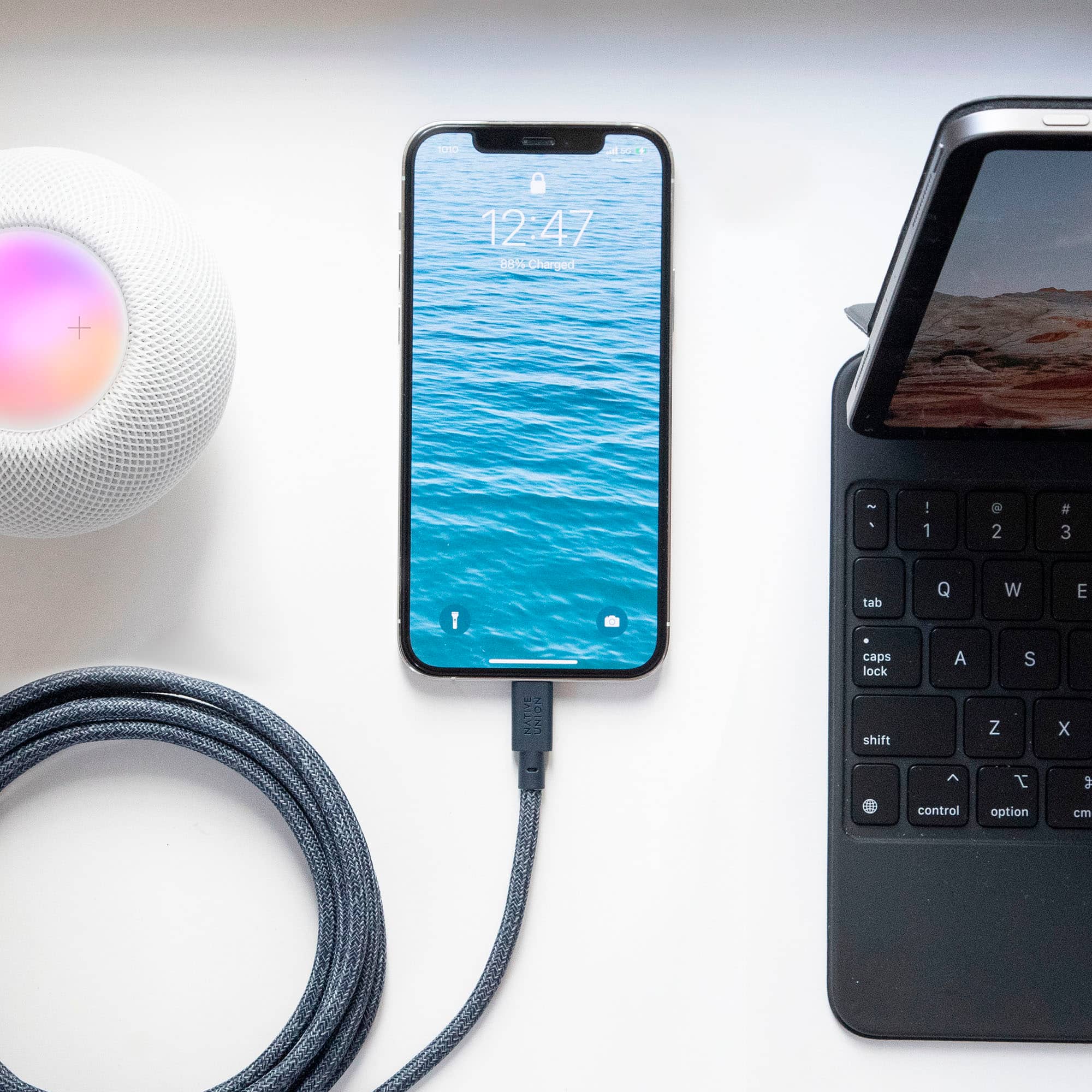 The image shows a smartphone that is connected to a computer with a cord. The phone is displaying the time of 12:47. The phone is also charging, as indicated by the charging cable. The image also shows a keyboard and a mouse, suggesting that the setup is for work or personal use.