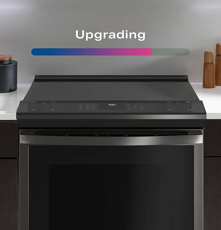 The image features a stainless steel oven with a black door, which is described as a gas range. The oven is placed in a kitchen setting, with a counter nearby. The oven is described as having a large screen, which might be used for displaying recipes or cooking instructions. Additionally, there are several bottles placed around the kitchen, possibly containing cooking ingredients or oils.