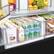 The image shows a refrigerator filled with various food items and drinks. There are several bottles of water, including Mineral Water, and a few bottles of juice. The refrigerator also contains some fruits, such as apples and oranges, as well as a broccoli. Additionally, there are some books placed in the refrigerator, possibly for reading during meal preparation or while enjoying a snack.