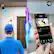The image features a man in a blue shirt and a blue cap, holding a cell phone with a 2-way audio app on the screen. The app allows the man to communicate with someone at the front door of his home. The image also includes a clock, indicating the time of the event. The man is likely using the app to monitor the situation or interact with someone at the door.