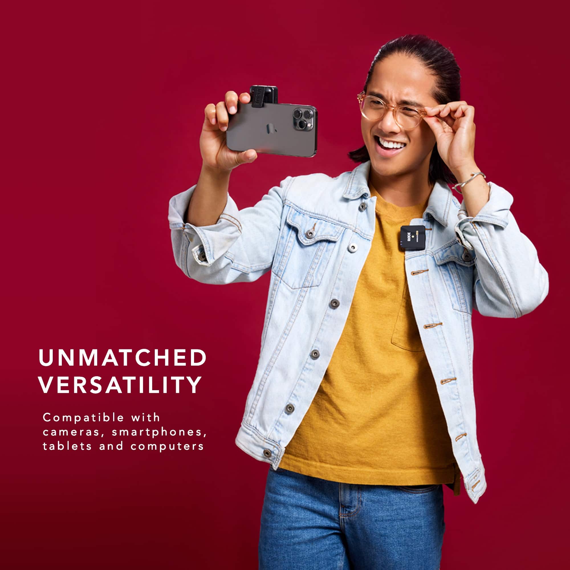 The image features a man wearing a blue jacket and holding a cell phone in front of a red background. The man is smiling, possibly taking a selfie or capturing a photo. The image is promoting the versatility of a product, which is compatible with various devices such as cameras, smartphones, tablets, and computers.