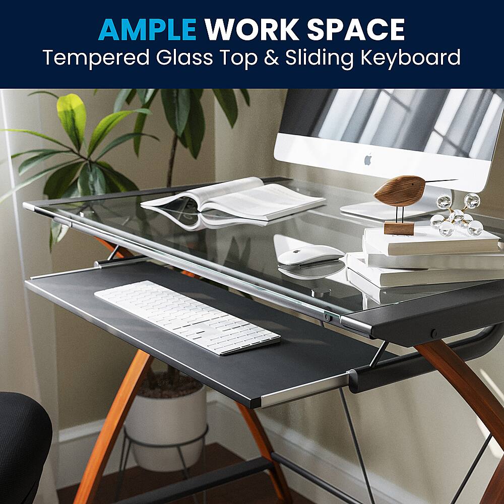 The image features a modern workspace with a tempered glass top desk. On top of the desk, there is a sliding keyboard, which adds a sleek and space-saving design to the setup. The desk also has a computer monitor, a mouse, and a potted plant nearby. Additionally, there are several books arranged on the desk, indicating a workspace that is both functional and aesthetically pleasing.
