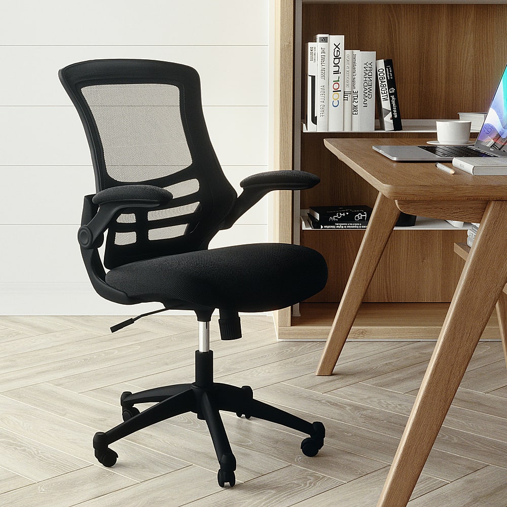 The image features a black office chair placed on a wooden floor. The chair is positioned in front of a wooden desk, which has a laptop and several books on it. The desk also has a cup and a keyboard. The scene appears to be a workspace or a study area.