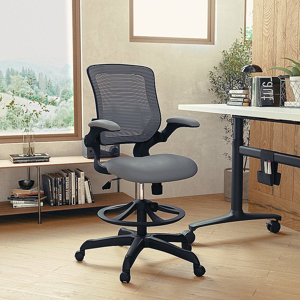 The image features a modern office chair with wheels, placed in front of a desk. The desk has a laptop on it, along with several books and a vase. There is also a potted plant nearby, adding a touch of greenery to the space. The office chair is positioned in front of a window, providing a view of the outdoors.