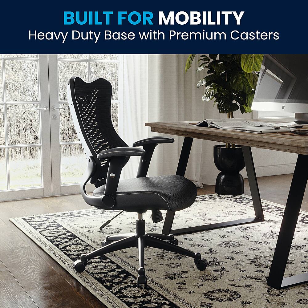 The image features a black office chair with a heavy-duty base and premium casters, placed on a rug in a room. The chair is positioned in front of a desk with a computer, keyboard, and mouse. There is also a potted plant nearby, adding a touch of greenery to the space. The scene suggests that the chair is designed for mobility and stability, making it suitable for use in various settings.