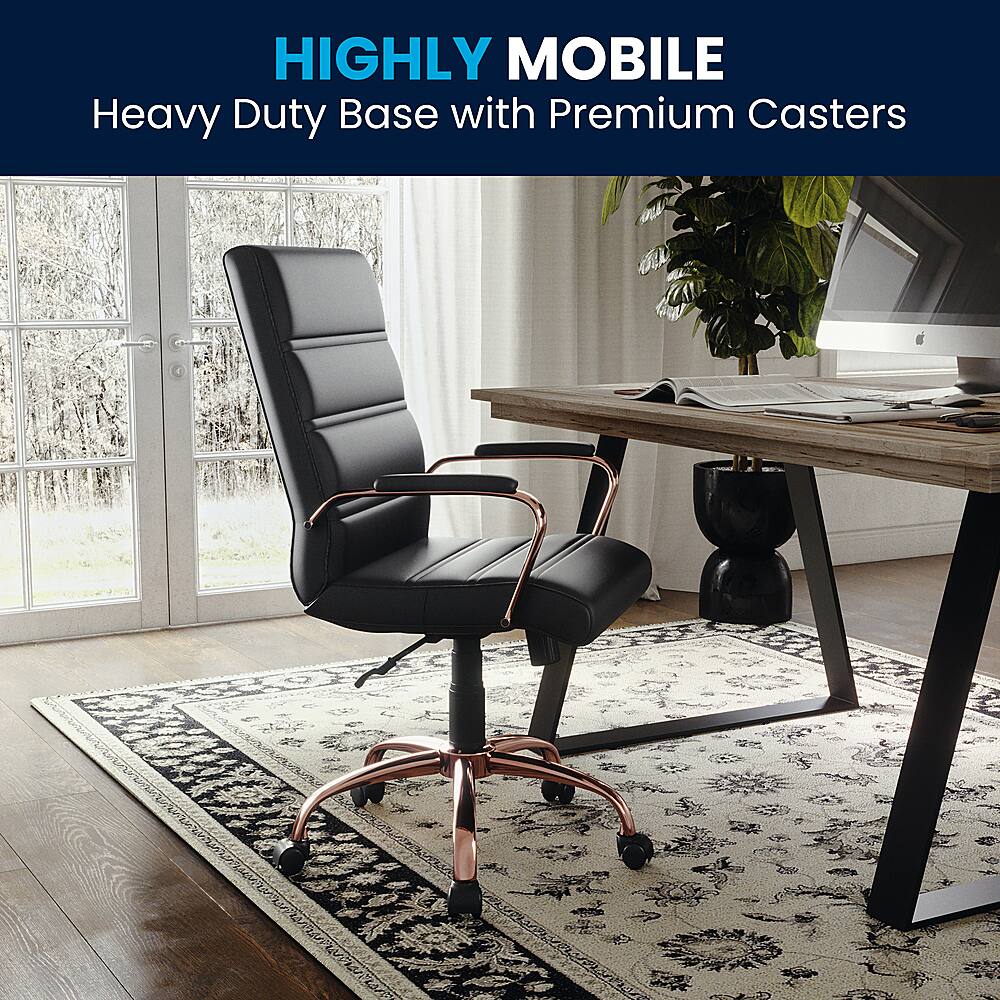 The image features a black office chair with a heavy duty base and premium casters. The chair is placed on a rug, and there is a desk nearby. The setting appears to be a home office or a workspace, with a potted plant and a TV in the background. The chair is designed to provide stability and durability, making it suitable for heavy use in a professional environment.