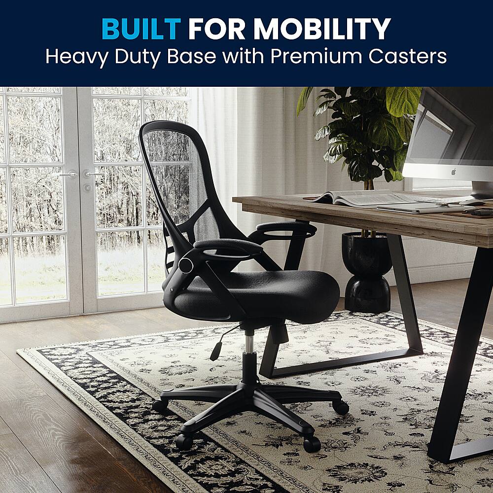 The image features a black office chair placed on a rug, with a wooden desk nearby. The chair is designed for mobility and has a heavy duty base with premium casters, making it easy to move around the room. The desk has a laptop and a keyboard on it, indicating that it is a workspace. Additionally, there is a potted plant and a TV in the room, adding to the overall ambiance and functionality of the space.