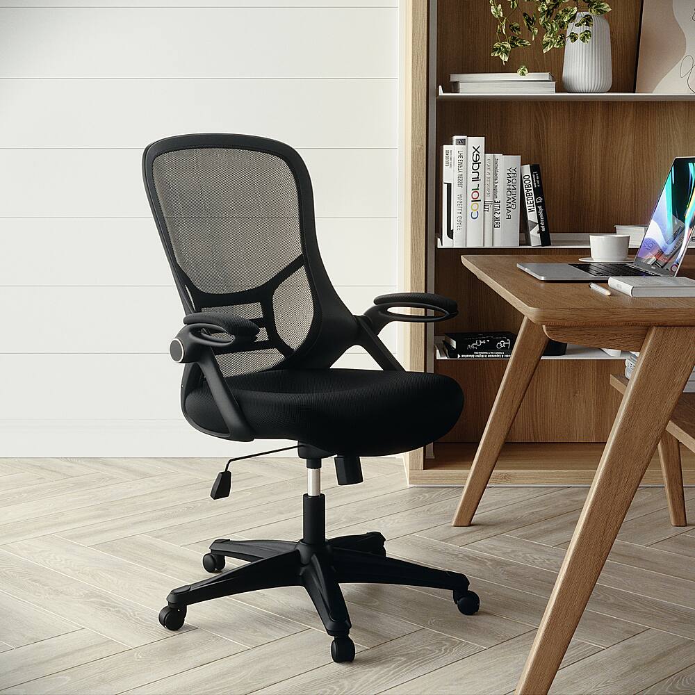 The image features a black office chair positioned in front of a wooden desk. The desk is equipped with a laptop, a keyboard, and several books. The chair is situated on a hardwood floor, and there is a potted plant nearby, adding a touch of greenery to the workspace. The overall scene conveys a professional and organized work environment.