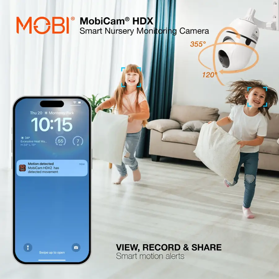 MobiCam HDX is a smart nursery monitoring camera that can detect motion and send alerts to your smartphone. The camera has a viewing angle of 355 degrees and can record and share footage with a resolution of 120. In the image, two children are playing in the room, and the camera is capturing their movements. The camera also has a feature that can detect excessive heat, ensuring the safety of the children.