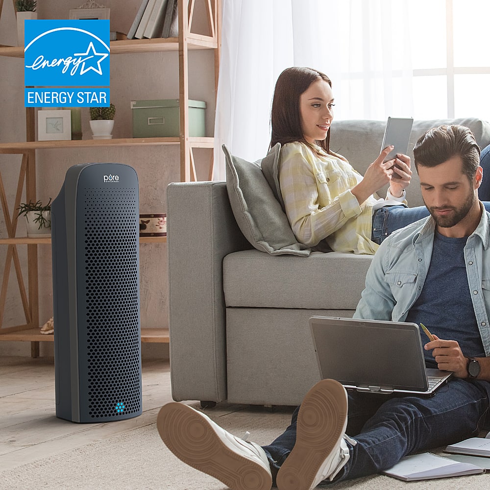 The image shows a man and a woman sitting on a couch, each using a laptop. They are surrounded by various items such as a potted plant, a vase, and a cup. The man is sitting on the floor with his laptop, while the woman is sitting on the couch. There is also a cell phone on the couch. The scene appears to be a cozy and comfortable living space where the couple can work or relax using their laptops.