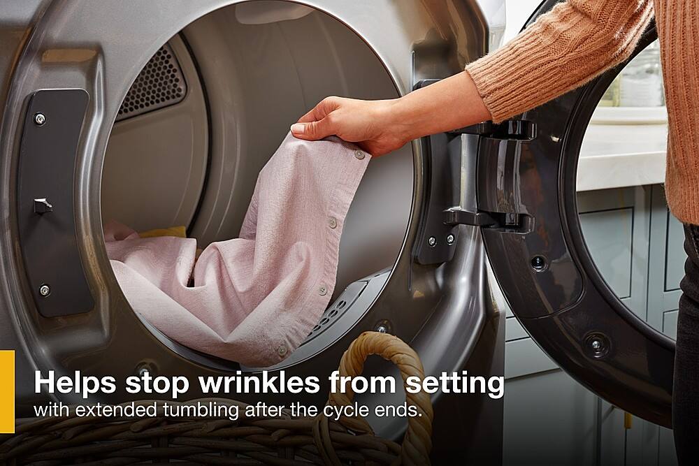 The image shows a person putting a shirt into a dryer, which is designed to help stop wrinkles from setting with extended tumbling after the cycle ends. The dryer is filled with clothes, and the person is in the process of placing the shirt inside. This helps to ensure that the clothes remain wrinkle-free and maintain their shape, making it easier for the person to have a neat and organized wardrobe.