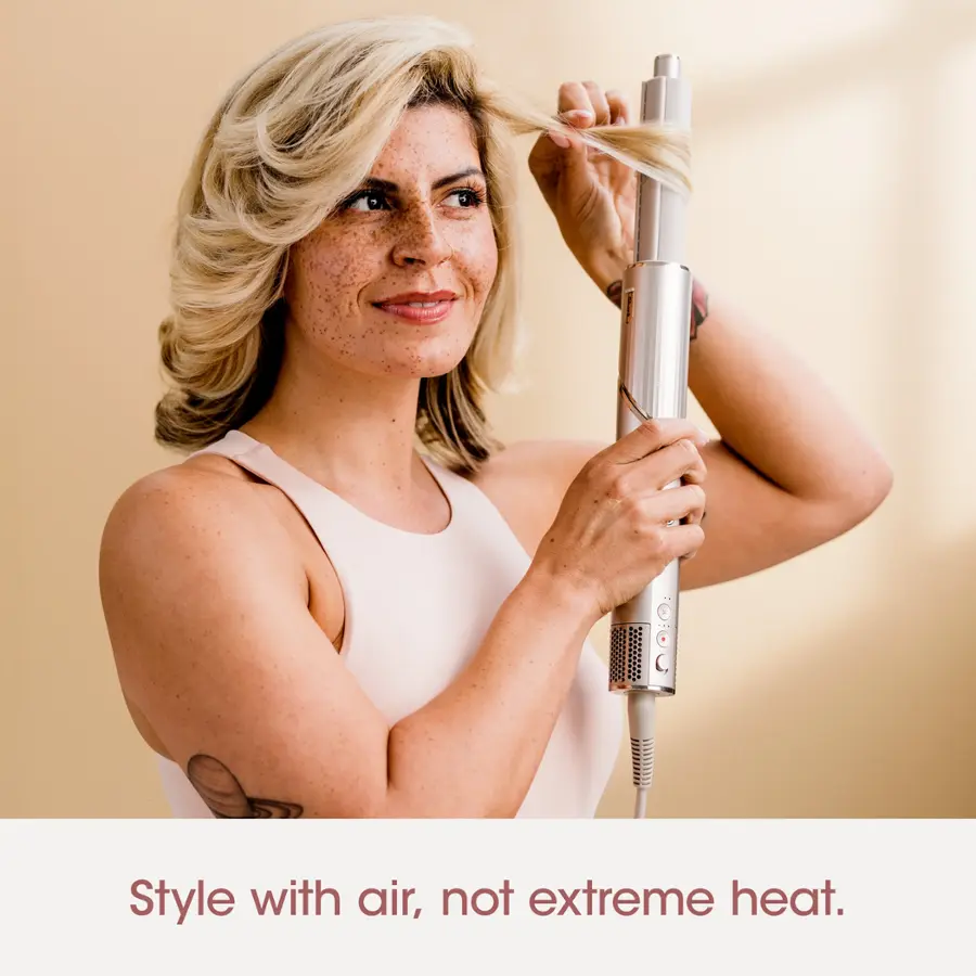 The image features a woman with blonde hair, wearing a white dress, and holding a hair dryer. The woman is smiling, possibly enjoying her time or the process of styling her hair. The text "Style with air, not extreme heat" suggests that using a hair dryer can be a more pleasant and less damaging way to style hair compared to using extreme heat.