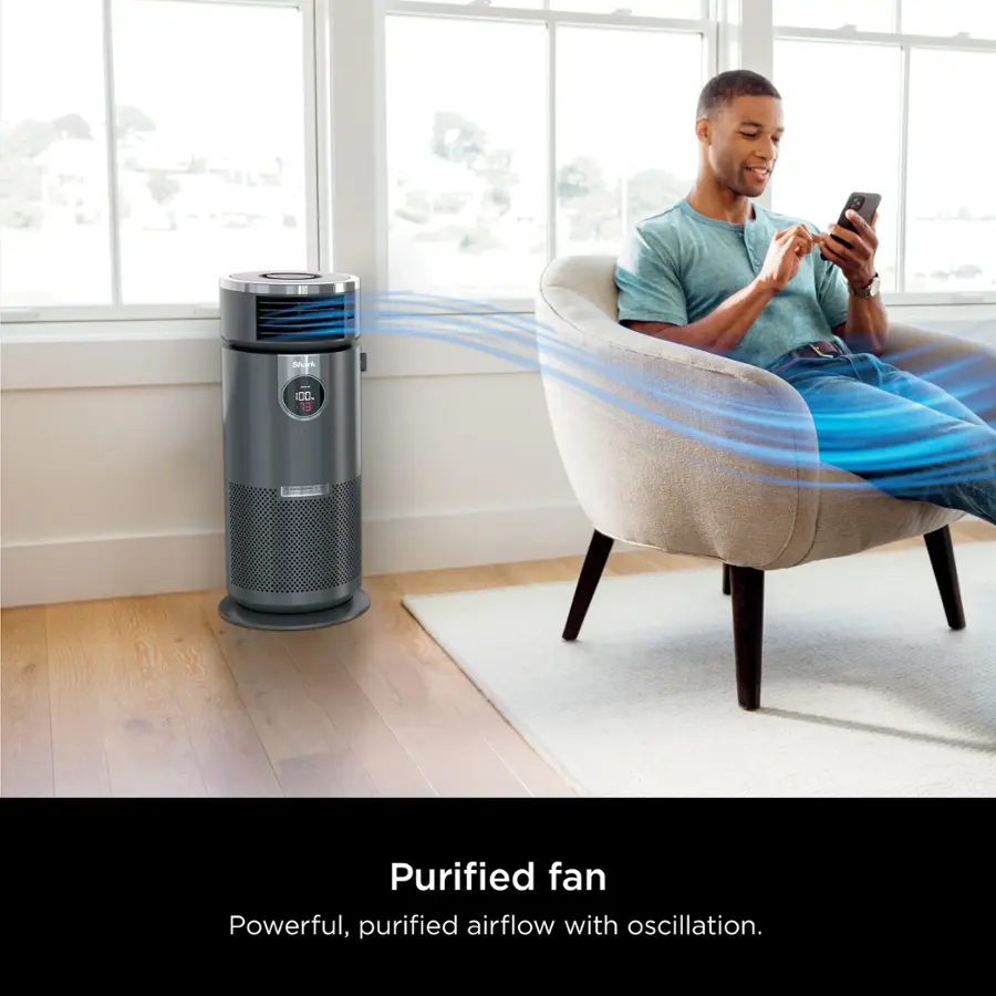 The image features a man sitting in a chair, holding a cell phone. There is a purified fan nearby, which is a powerful and purified airflow with oscillation. The man appears to be engaged with his phone, possibly texting or browsing the internet.