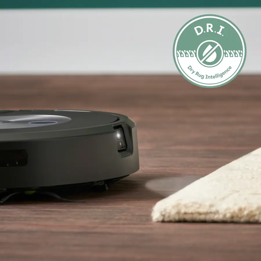 The image features a robotic vacuum cleaner sitting on a wooden floor. The vacuum is black and has a circular shape. It is positioned on a rug, which is placed on the wooden floor. The vacuum is likely a part of a smart home system, as it is described as "D.R.I. A DODY Dry Intelligence Rug." The presence of the D.R.I. logo suggests that the vacuum is an intelligent and advanced device.