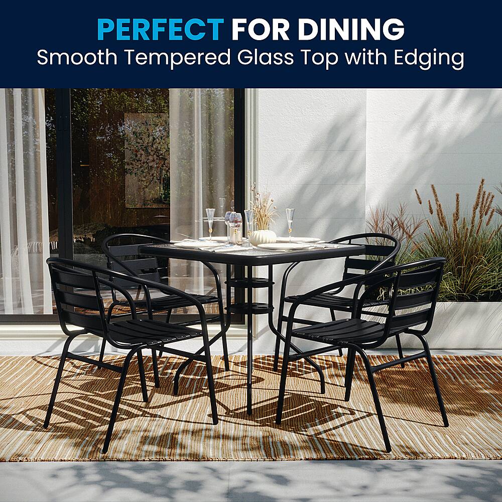 The image showcases a dining table set with four chairs, a glass top, and a vase. The table is surrounded by chairs, and the glass top adds a touch of elegance to the setting. The table is set for a meal, making it perfect for dining. The smooth tempered glass top with edging enhances the overall aesthetic of the table, creating a visually appealing and comfortable dining experience.