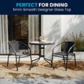 The image features a dining table with a 5mm smooth designer glass top, surrounded by four chairs. The table is set with a wine glass and a vase, creating a pleasant and inviting atmosphere for a meal. The glass top adds a touch of elegance and sophistication to the dining experience.