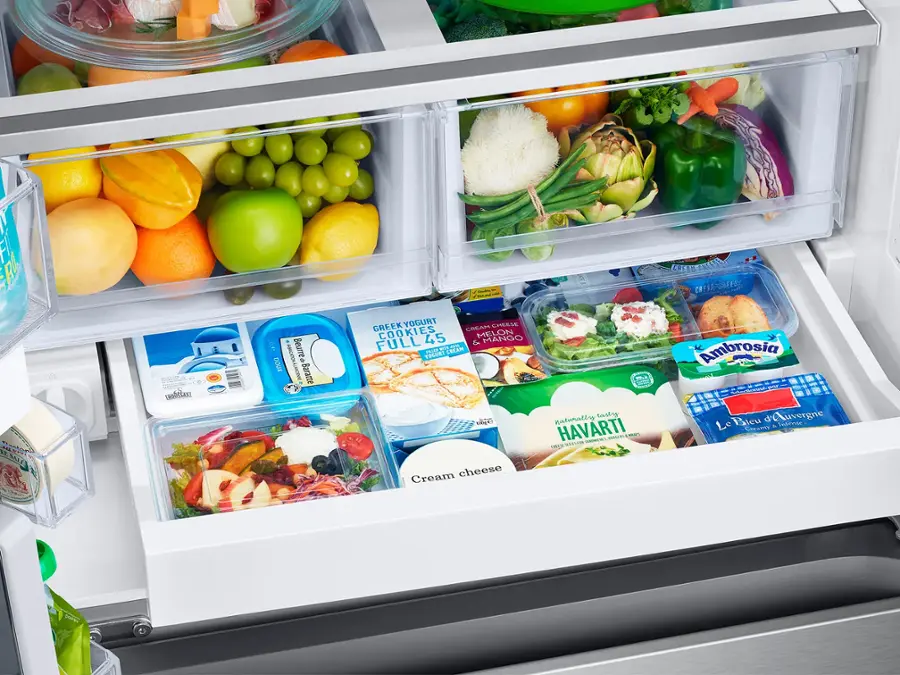 The image shows a refrigerator with its door open, revealing a variety of food items inside. There are several apples, oranges, and carrots placed in different compartments of the refrigerator. Additionally, there are multiple bottles, including a bottle of wine, and a bowl. The refrigerator is well-stocked with a diverse selection of food items, making it a convenient and accessible source of nourishment for the household.