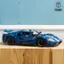 The image showcases a blue toy car being assembled with various parts. The car is a Ford GT, and it is being built using Legos. The car is being put together by a person who is carefully attaching the parts to create the final product. The toy car is displayed on a table, and it is the main focus of the image.