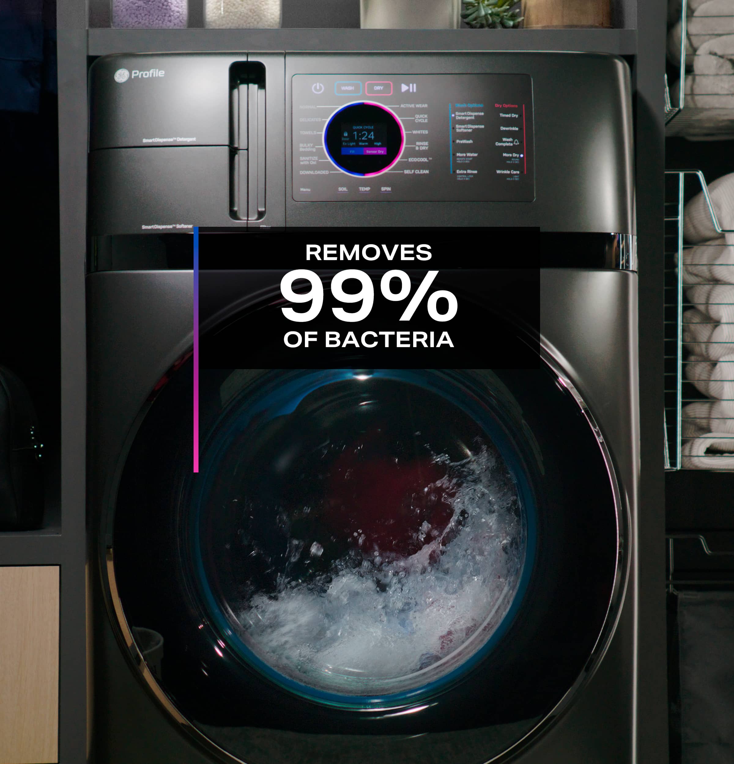 The image features a large washing machine with a clear door, showcasing the interior of the machine. The machine is advertised as removing 99% of bacteria, making it a hygienic option for laundry. The machine is placed next to a shelf with towels, indicating that it is likely used in a laundry room or a similar setting.