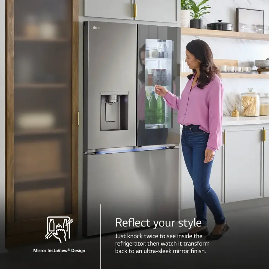 The image features a woman standing in front of a large refrigerator with a mirrored door. She is opening the door, which has a mirrored surface that allows her to see inside the refrigerator. The refrigerator is part of the LG Mirror InstaView Design, which reflects the user's style and provides a sleek mirror finish. The woman is wearing a pink shirt and jeans, and there are several bottles and a bowl visible in the scene.