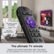 The ultimate TV remote is a hands-free device that allows users to search and control their TV using voice commands. It is rechargeable and even comes with a lost remote finder. The image shows a close-up of the remote control, which is purple and black in color. The remote is placed in front of a TV, and there is a potted plant nearby. The remote control is designed to work with Roku, a popular streaming device.