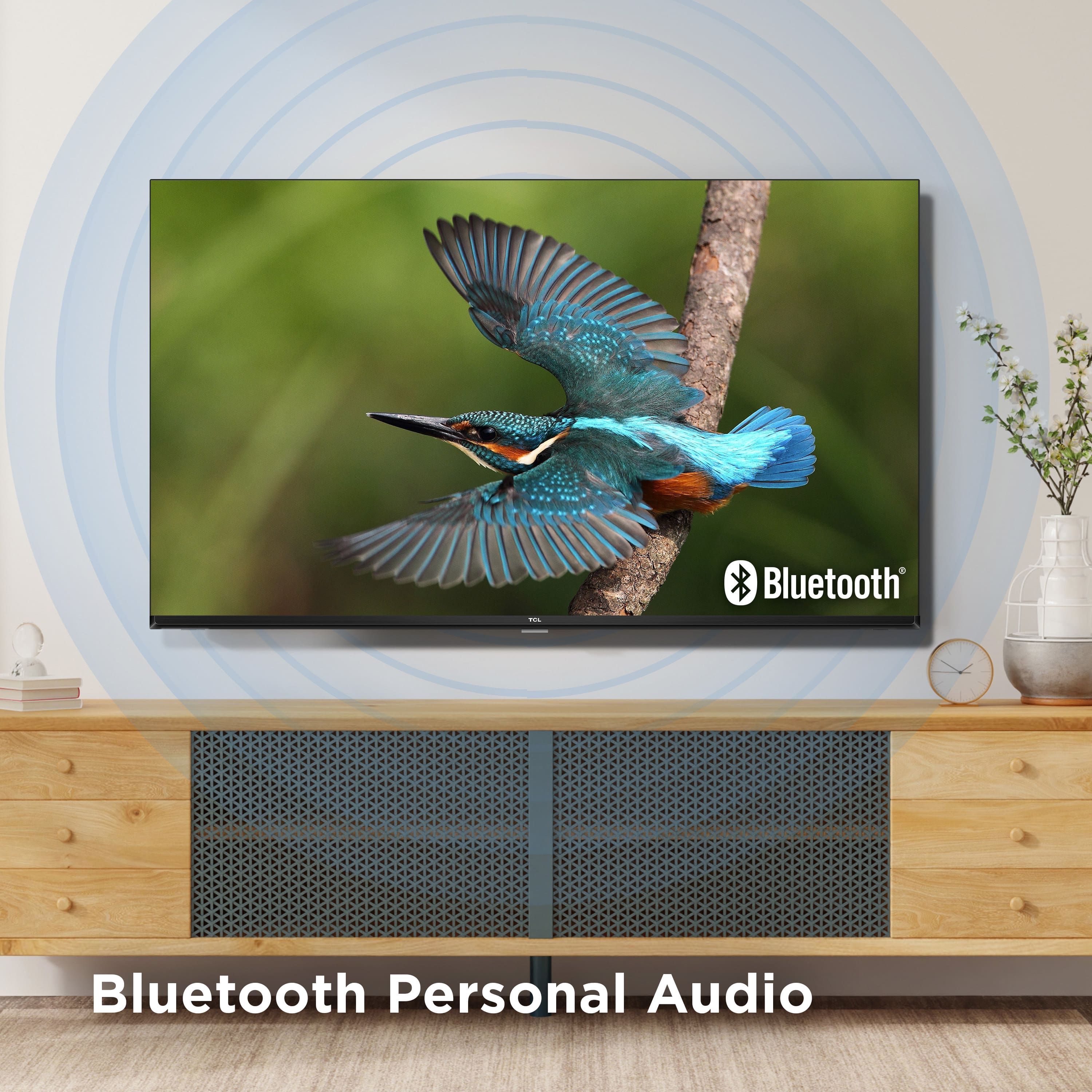 The image features a large flat screen television with a blue bird perched on a tree branch in the foreground. The television is advertising Bluetooth Personal Audio, which is likely a feature of the TV. The television is placed on a wooden stand, and there are a few potted plants nearby, adding a touch of greenery to the scene.