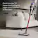 The image shows a person holding a red and black vacuum cleaner, specifically a Digital Motorbar XL, while cleaning a white carpet. The vacuum cleaner is designed to intelligently adapt its power based on the type of floor it is being used on, making it suitable for all floor types. The person is standing in a living room, with a couch visible in the background.