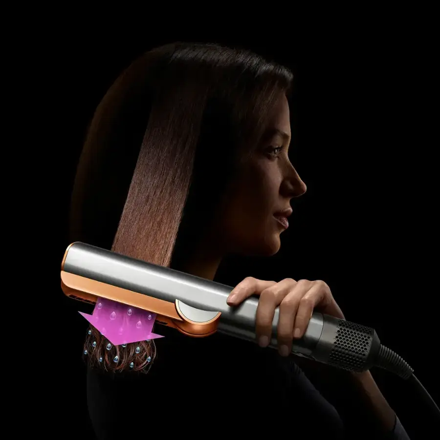 The image showcases a hair straightener with a purple light on it. The text reads, "Straighten from dry Touches up dry hair with directional airflow to smooth and align hair for a refreshed style." The hair straightener is designed to work on dry hair, providing a smooth and aligned finish for a refreshed look.