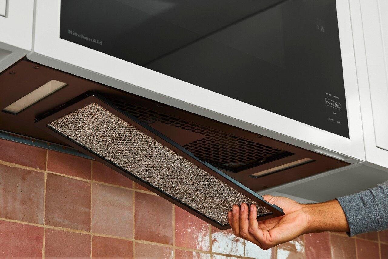 The image shows a person holding a red and white towel in a microwave oven. The microwave is open, and the towel is being placed inside. The person is likely preparing to heat the towel or use it for a specific purpose. The microwave is a common appliance used for heating food and other items, and in this case, it is being used for heating a towel.