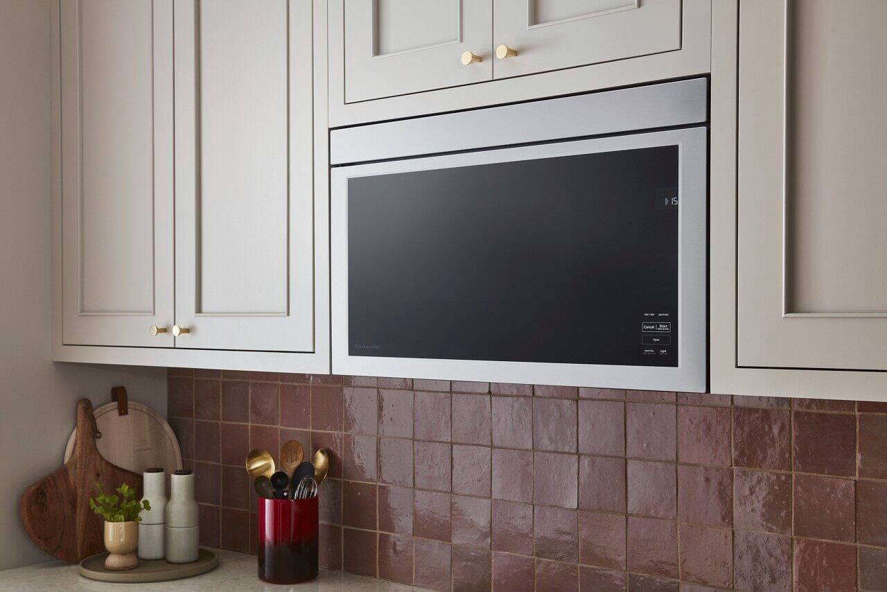 The image shows a modern, stainless steel microwave oven with a black screen. The microwave is placed on a white background, making it stand out. The oven is designed to be built into a wall, and it has a sleek, contemporary appearance.